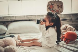 可爱的小女孩拿着相机坐在床上