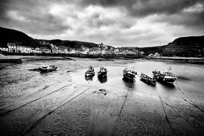 一个Black and white landscape photo of a line of boats sitting in harbour at low tide