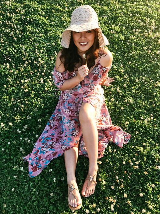 桃红色华丽的礼服和草帽的女孩坐草和拿着一朵白花在她的下巴下在智能手机时尚摄影射击的一个明亮的天