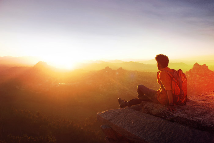 一个背包客坐在悬崖边看日落的照片。光度计摄影技巧