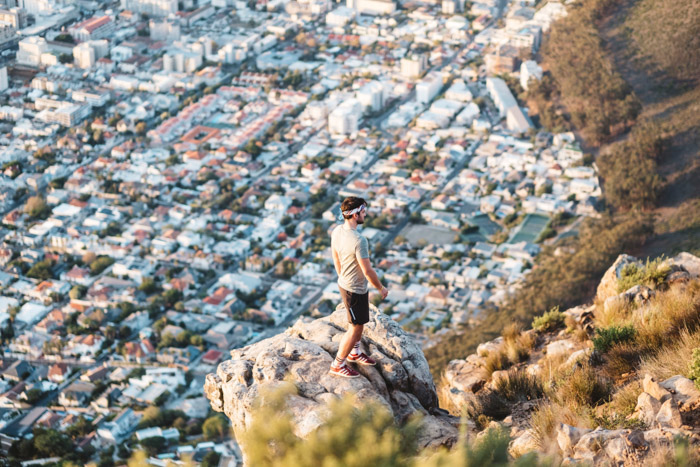 A man standing on the edge of a cliff with an impressive view of houses and buildings below - compositional photography rules