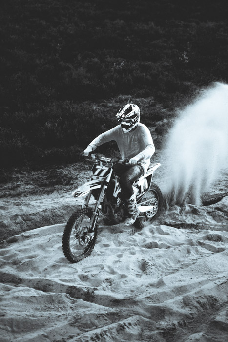 一张黑白照片，一个男人骑着自行车穿过沙滩。他显然是这张照片的主要焦点。