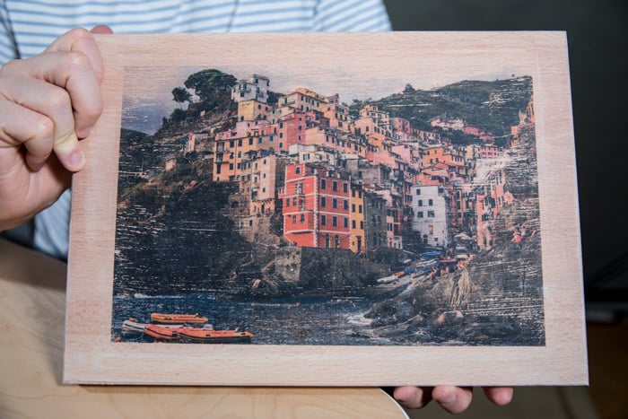 一个男人拿着一块木板，上面转移着一张五颜六色的海滨小镇的照片