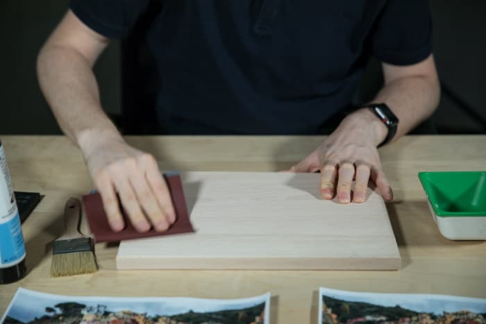 一个男人坐在一张木桌，打磨木板准备表面以便将照片转移到木材