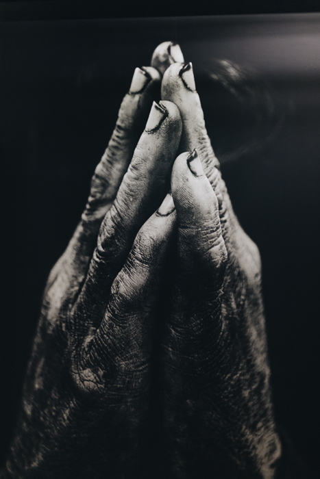 这是一张黑白胶片照片，照片中一个人双手合十，做着“祈祷”的手势