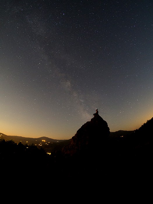 一个人坐一个岩石在令人印象深刻的星填装的天空下