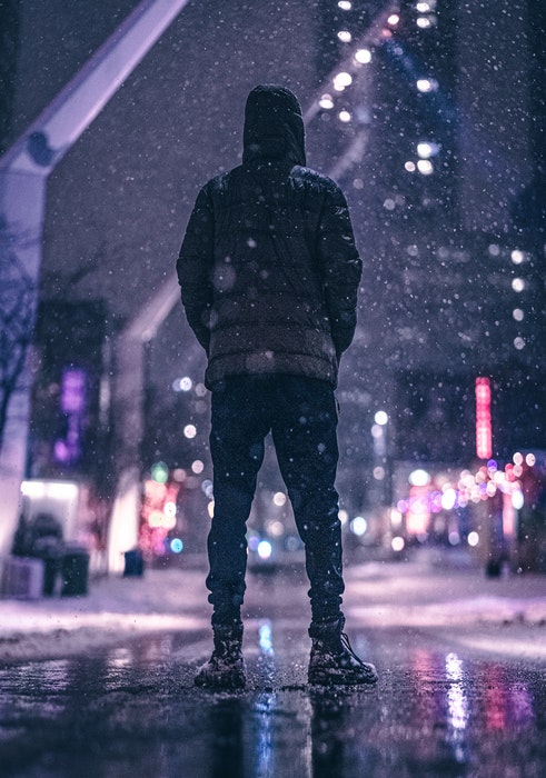 一个穿着冬衣的男人站在下雪的城市街道上