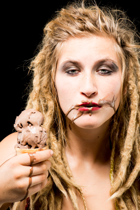 一个金发女孩与巧克力冰淇淋在她的脸上对着一个黑色的背景-照片道具
