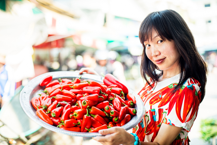 年轻漂亮的亚洲女人在户外市场吃着红辣椒。——摄影道具